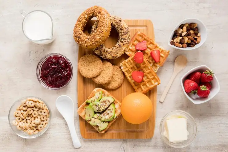 High-protein breakfast for energy with orange cake, strawberries, dried fruits, nuts, milk, avocado toast, butter, jam, and cereal